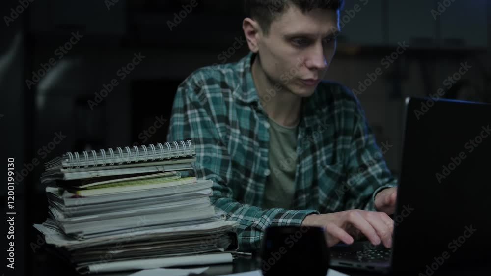 Focused and concentrated guy student e learning online on internet website. Young man working remotely at home office desk, makes notes in work document, looks at laptop computer