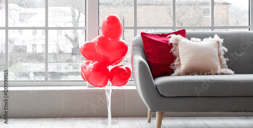 Interior of living room with grey sofa and heart-shaped balloons near window. Valentine's Day celebration photo