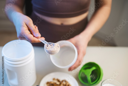 Wallpaper Mural Athletic woman in sportswear preparing protein drink in a kitchen, putting a portion of whey protein powder from a measuring spoon into a shaker in her hand Torontodigital.ca