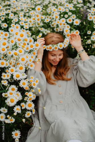 A young woman in a flowy dress and headband walks through a blooming daisy field, enjoying the peaceful countryside atmosphere under a cloudy sky.
