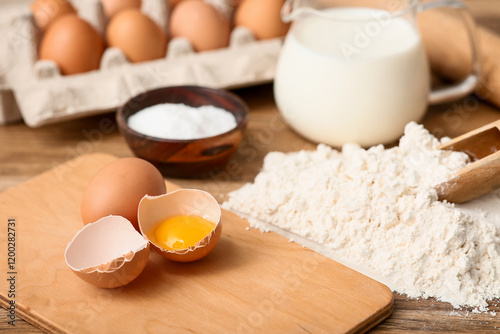 Heap of flour with eggs, jug of milk, scoop and salt for preparing dough on wooden background