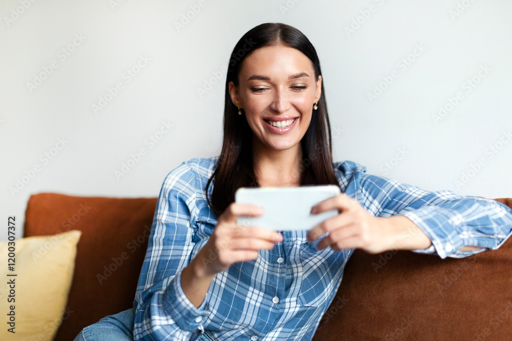 Joyful woman playing mobile game on smartphone, resting and having fun at free time on comfy couch at home, lady feeling happy and relax Joyful woman playing mobile game on smartphone, resting and having fun at free time on comfy couch at home, lady feeling happy and relax