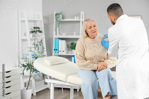 Male doctor examining mature woman's shoulder in clinic photo