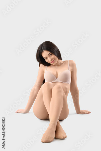 Attractive young woman in beige tights sitting on light background