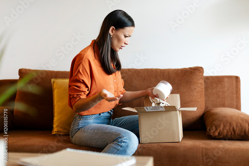 Discontented woman buyer unpacking cardboard box with incorrect product, sitting on sofa at home. Delivery service and shopping problems
