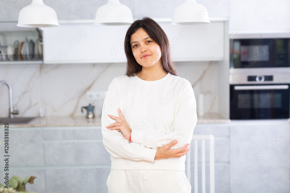 Positive confident young dark-haired woman in white casual jumper posing in stylish home kitchen.. Positive confident young dark-haired woman in white casual jumper posing in stylish home kitchen..