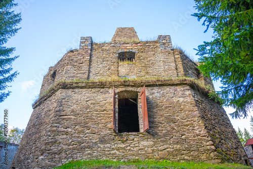 The remnants of a historic lime kiln stand near Kovarska, surrounded by lush greenery. The structure features large openings and aged stones, reflecting its industrial past in the Ore Mountains.