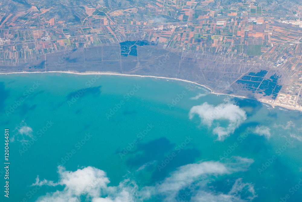 Stunning aerial view of coastline featuring turquoise waters, scattered clouds, and a patchwork of fields. Serene ocean contrasts with the structured land, creating a harmonious natural landscape