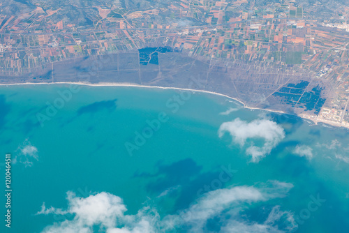 Obraz na płótnie Stunning aerial view of coastline featuring turquoise waters, scattered clouds, and a patchwork of fields. Serene ocean contrasts with the structured land, creating a harmonious natural landscape w salonie
