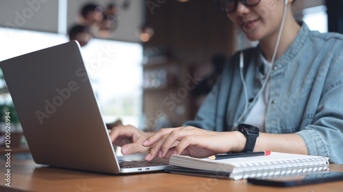 Business woman wearing earphone, working on laptop computer, video conference via online meeting app at coffee shop. Student studying online class via laptop, surfing the internet, freelance at work