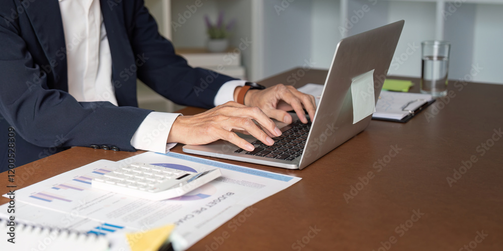 Elderly businessman typing on a laptop while analyzing financial data in an office