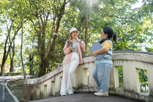 Diverse friends conversing on a bridge in a sunny park, sharing ideas with tablets in hand photo