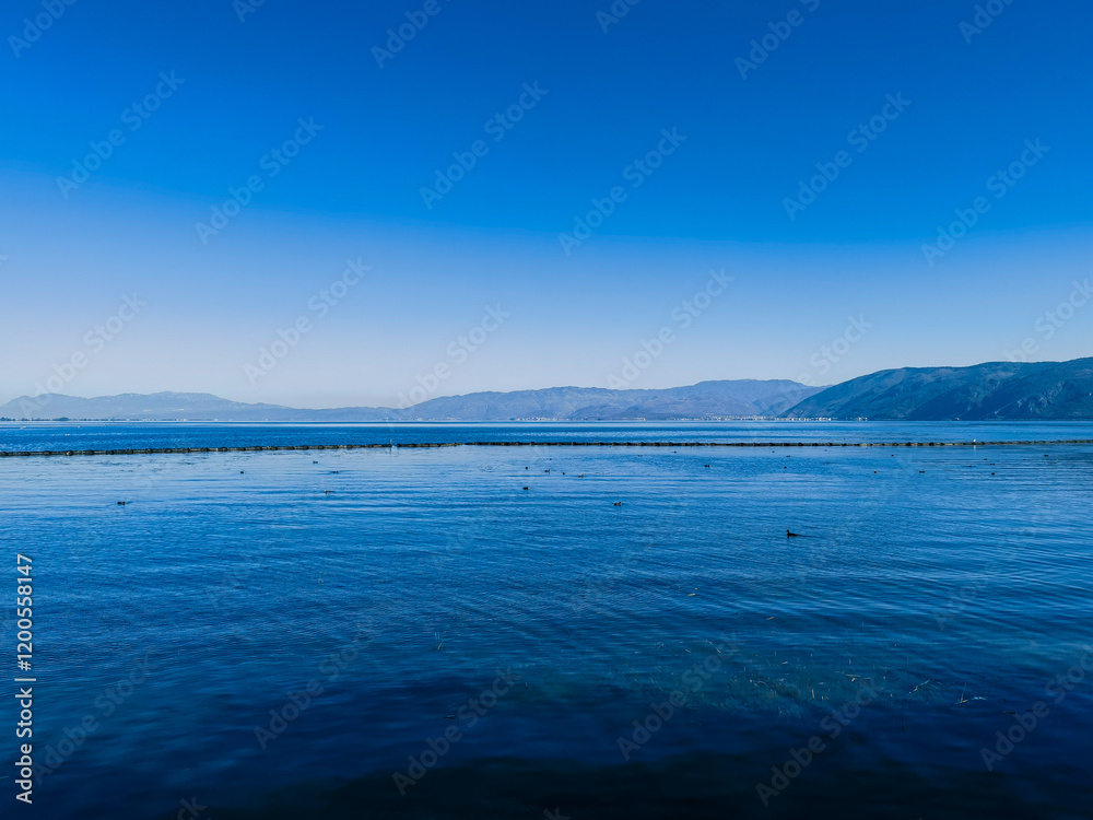 Serene lake under a vibrant blue sky. Distant mountains create a tranquil horizon. Calm water reflects the sky. A peaceful, idyllic landscape. Serene lake under a vibrant blue sky. Distant mountains create a tranquil horizon. Calm water reflects the sky. A peaceful, idyllic landscape.