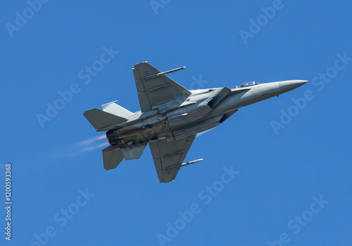 Military jet soaring through a clear blue sky, showcasing power and speed with minimal cloud cover.