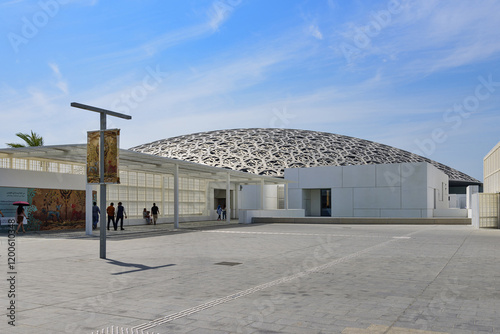 Abu Dhabi, United Arab Emirates - April 28, 2024: Wide angle of square and tourists walking on lobby toward entrance door and arch roof of Louvre Museum photo