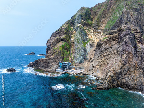 Dokdo Island, Ulleung-gun, Gyeongsangbuk-do, South Korea - May 26, 2024: High angle and spring view of sea wave with a building under rock cliff at Seodo Island photo