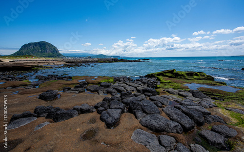 Spring view of pool at low tide with green laver on volcanic rocks against Sanbangsan Mountain and horizon at Sagye Beach of Seogwipo-si, Jeju-do, South Korea photo