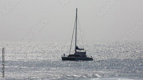 Seogwipo-si, Jeju-do, South Korea - August 1, 2020: High angle and silhouette view of a yacht with tourists sailing on the sea with sunlight against light fog and horizon photo