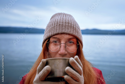 Pretty smiling female traveler drinking from thermos outdoors