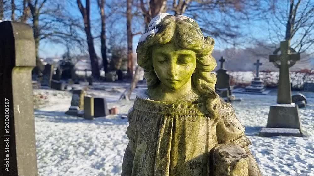 Weathered cemetery angel child statue sunlit in snowy graveyard at sunrise slowly moving left Weathered cemetery angel child statue sunlit in snowy graveyard at sunrise slowly moving left