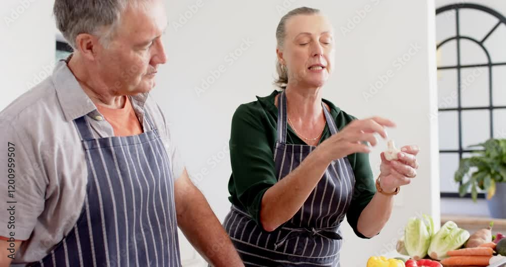 Senior friends in kitchen, woman explaining cooking technique to man