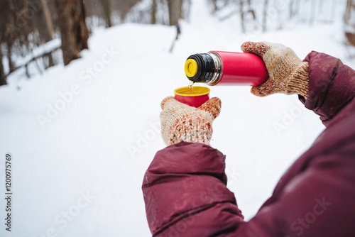 In a snowy environment, a person is carefully pouring a warm beverage from a thermos into a cup, enjoying the peaceful winter scenery around them while staying warm and cozy photo