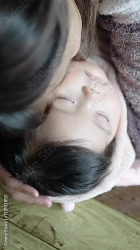 A 6-month-old Japanese girl and her mother wearing fluffy clothes in a warm winter Japanese apartment room. Trying to put the baby on the desk. Vertical slow motion video. photo