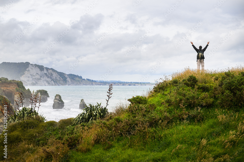 Man raising arms on clifftop and looking at the views of Three Sisters rock formation. Tongaporutu. Taranaki. New Zealand. Man raising arms on clifftop and looking at the views of Three Sisters rock formation. Tongaporutu. Taranaki. New Zealand.