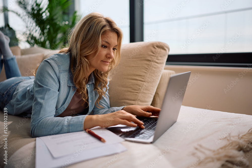 Mid adult woman working on computer while relaxing on sofa. Mid adult woman working on computer while relaxing on sofa.
