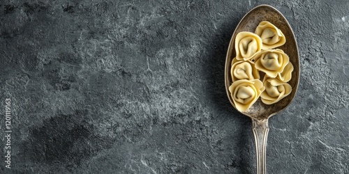 Handmade Italian tortellini and ravioli on a vintage spoon, set on a textured grey background with ample copyspace to the right for text.