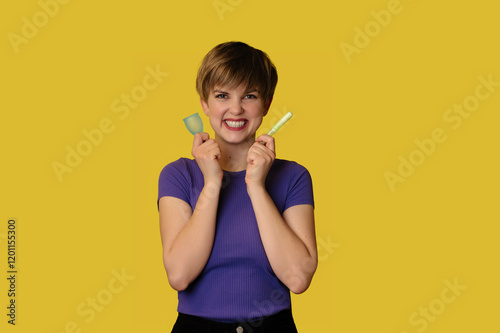 A smiling woman dressed in casual clothes holds a silicone menstrual cup and a tampon highlighted on a yellow background. The medical concept of menstruation days for gynecologists and PMS. photo