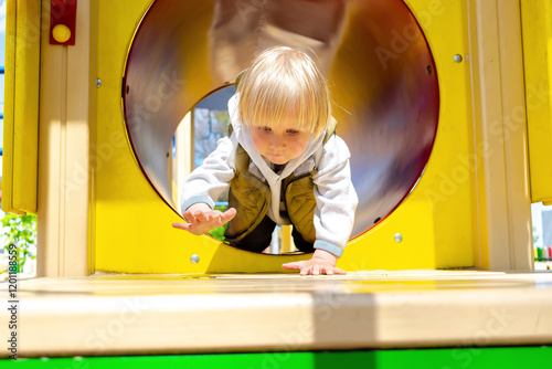 Cute blond little toddler kid child boy crawling climbing through tunnel,pipe in playground.Children physical development and childhood daycare, kindergarten concept
