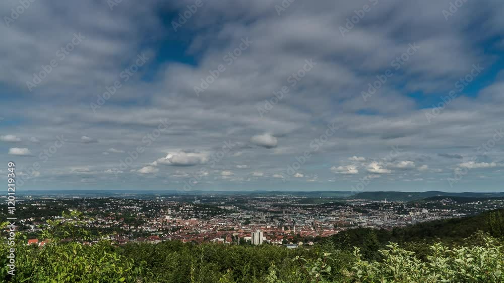 A captivating time-lapse of Stuttgart from a surrounding hill, with the city nestled in the valley below. Fluffy clouds drift across the sky, creating a peaceful atmosphere over the urban landscape A captivating time-lapse of Stuttgart from a surrounding hill, with the city nestled in the valley below. Fluffy clouds drift across the sky, creating a peaceful atmosphere over the urban landscape
