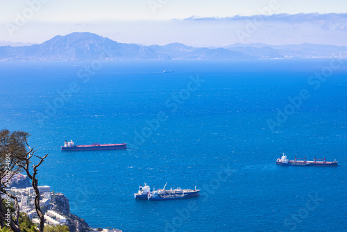 View from Gibraltar, British Overseas Territory on the Iberian Peninsula. Cargo ships at sea with distant mountains visible on the horizon. A tranquil ocean scene.