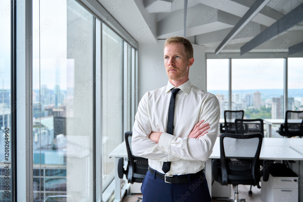 Fototapeta premium Serious young professional business man, confident executive ceo manager, rich male investor wearing tie standing crossing arms in office looking away through skyscraper window thinking of future.