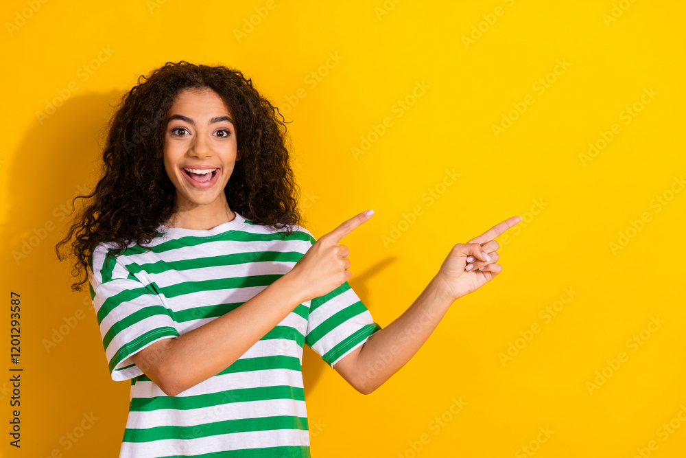 Portrait of pretty young girl indicate fingers empty space wear striped t-shirt isolated on yellow color background Portrait of pretty young girl indicate fingers empty space wear striped t-shirt isolated on yellow color background