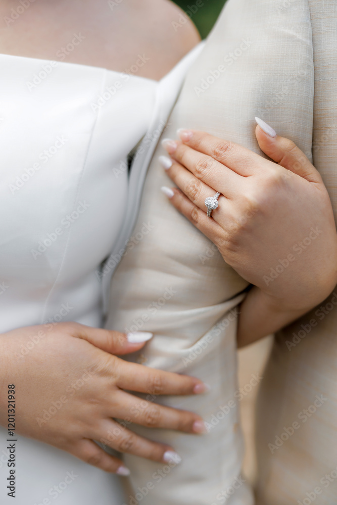 Close-up of the bride's hands hugging the groom's arm. Cropped photo of the hands of the bride and groom on their wedding day. The bride in her wedding ring hugs and crosses her arms with the groom Close-up of the bride's hands hugging the groom's arm. Cropped photo of the hands of the bride and groom on their wedding day. The bride in her wedding ring hugs and crosses her arms with the groom