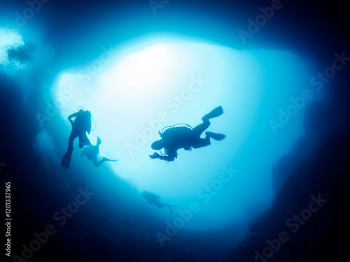 silhouette of unrecognizable scuba diver doing ok symbol with hand while swimming in dark cave undersea in deep clear water, concept of active leisure and underwater adventure
