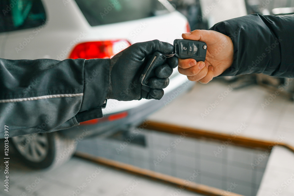 Mechanic wearing gloves handing over car keys to a customer in an auto repair shop, with a white car in the background Mechanic wearing gloves handing over car keys to a customer in an auto repair shop, with a white car in the background
