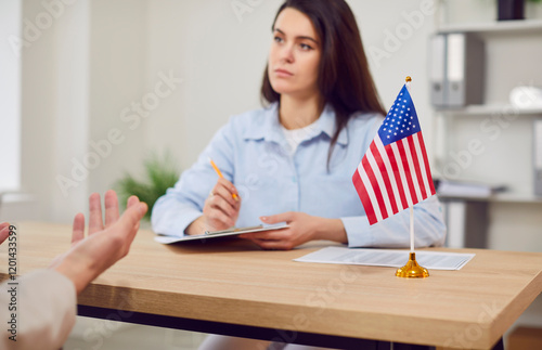 Foto Male person sitting in the office of the US public services or embassy having consular visa interview with a young pretty woman officer with US flag at the desk of official's workplace