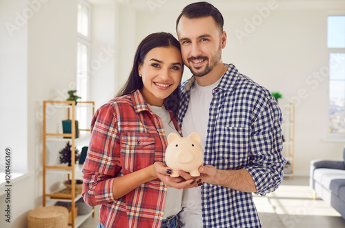 Happy young couple is holding piggy bank to save money to fulfill their future dreams. Beautiful Caucasian married couple posing at home with pig shaped piggy bank. Concept of saving money. photo