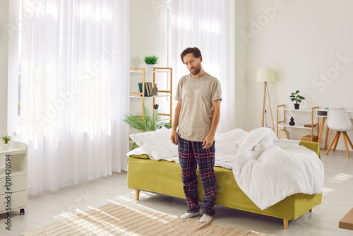 Young sleepy man somnambulist person suffering from sleepwalking standing with closed eyes near his bed. Male sleepwalker wearing pajamas at home. Somnambulism, insomnia and sleep problems concept. photo