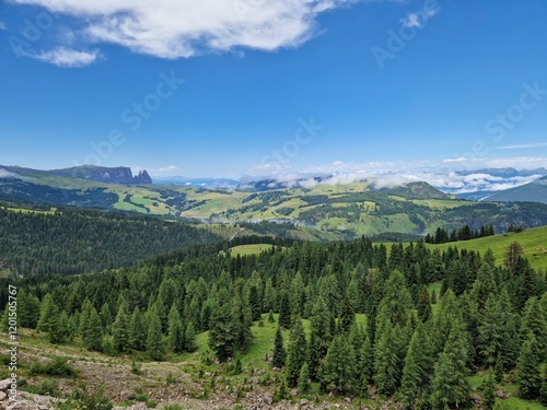 Idyllic mountain valley view, Italian Dolomites, rolling green hills and lush forests under a clear blue sky, mountains in the distant