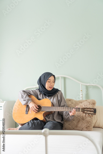 Moslem teenager woman learn play guitar focused bed room copy text space vertical photo