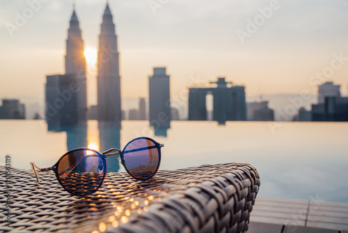 Canvas Print Fancy sunglasses forgotten on sanbed next to infinity pool with two skyscrapers tower twins reflected on water surface during evening sunset time