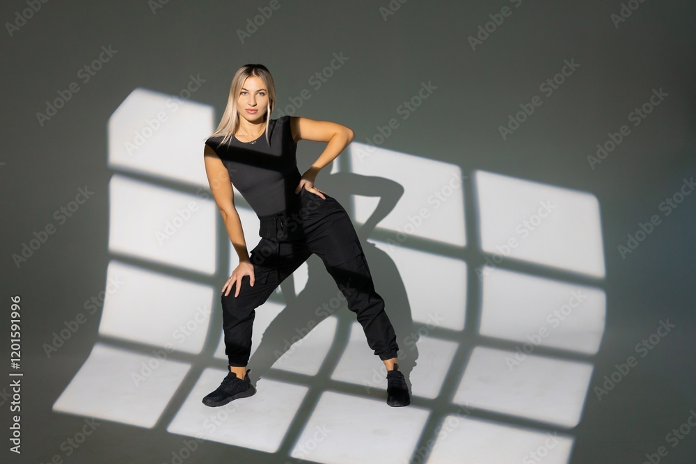 Fototapeta premium Dancer posing in studio with window light shadows, wearing black clothes