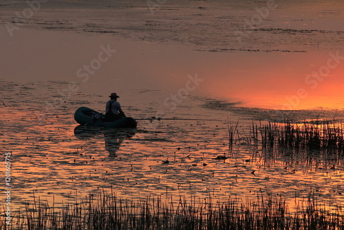 A man catches fish on an inflatable boat on the river in the evening with the setting sun. A beautiful evening in nature to relax while fishing. Calmness from the noise of city life