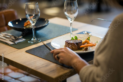 Fototapeta Naklejka Na Ścianę i Meble -  Une femme de dos mange un plat gastronomique à base de viande et de patate, elle tient dans ses mains une fourchette et un couteau
