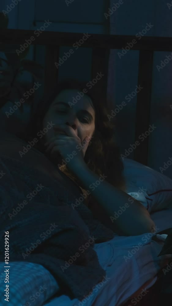 Vertical video. Sleepy woman wakes up early on weekday morning before dawn on an alarm clock.