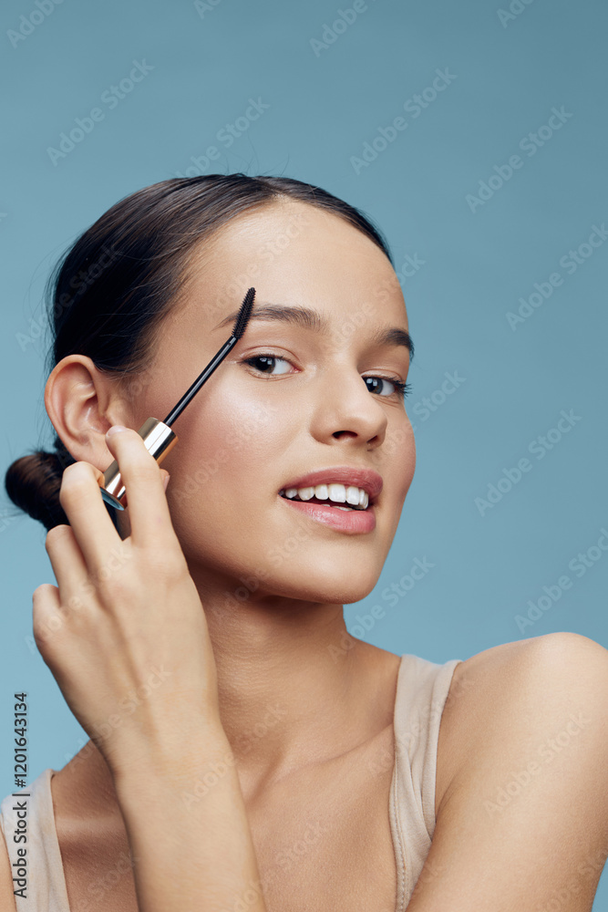 Young woman applying brow makeup against a light blue background, showcasing confidence and beauty with natural skincare and elegant style Young woman applying brow makeup against a light blue background, showcasing confidence and beauty with natural skincare and elegant style